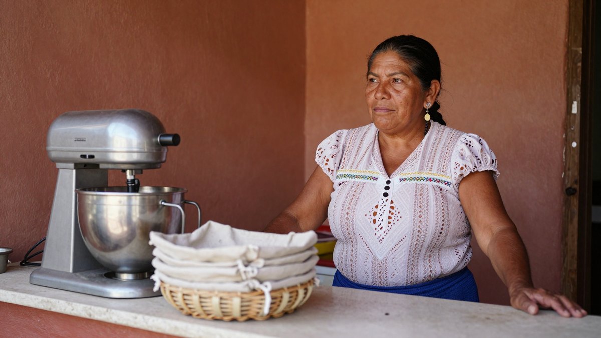 Mujer mexicana de mediana edad dentro de su tortillería, junto a canasta con paños y batidora